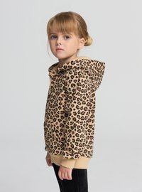 Bluza z kapturem w beżowy wzór w cętki, z czarnymi akcentami, z przednią kieszenią i ściągaczami na rękawach, noszona przez dziewczynę.