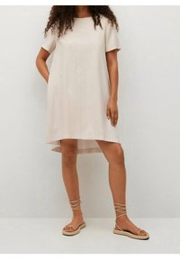 Vestido beige de manga corta con un dobladillo asimétrico y una textura suave, combinado con sandalias beige con tiras.