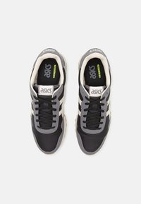 Black and gray athletic shoes with a smooth texture, featuring a textile upper, laces, and white side stripes. Asics logo on the tongue.