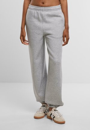 Svetlo šedé tepláky vyrobené z jemnej tkaniny, s elastickým pásom a manžetami na nohách, ponúkajúce voľný strih a bočné vrecká.