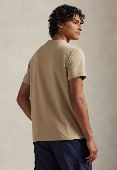 Μπεζ βαμβακερό t-shirt με κοντά μανίκια, στρογγυλή λαιμόκοψη και άνετη γραμμή. Διαθέτει λεία υφή και διακριτικές ραφές.