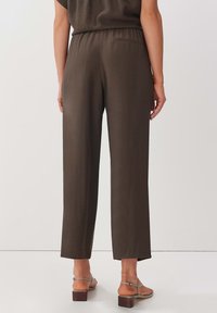 Pantalons marron amples avec une taille élastique et une poche latérale. Texture lisse, jambes droites et coupe au niveau des chevilles.