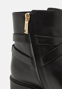 Černá kožená kotníková bota s bočním zipem, horizontálními popruhy a texturovaným povrchem pro sofistikovaný, strukturovaný design.