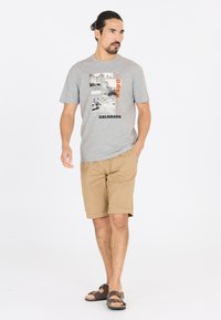 Harmaa puuvillapaita, jossa on Colorado-teemainen graafinen printti, yhdistettynä vaaleanruskeisiin shortseihin ja ruskeisiin sandaaleihin; rento malli ja käännetyt shortsien lahkeet.