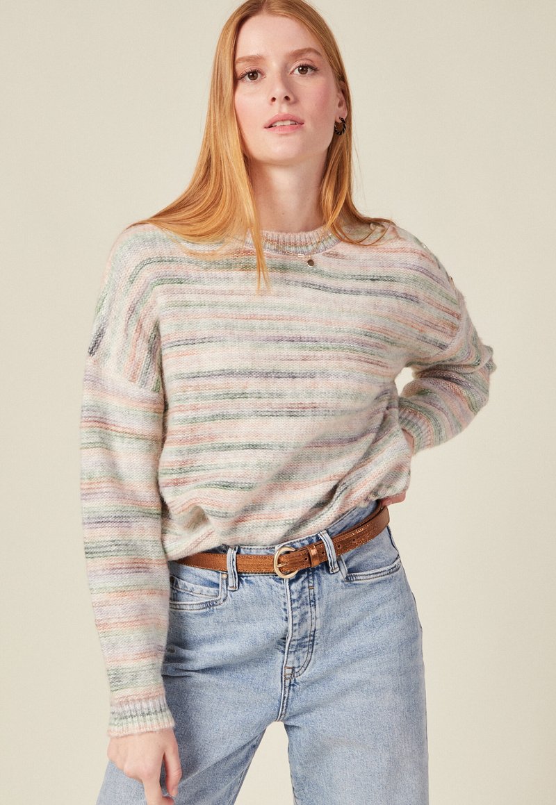 Mehrfarbiger Strickpullover mit horizontalen Streifen in pastellfarbenen Tönen, rundem Halsausschnitt und lockerer Passform, kombiniert mit hellblauen Jeans und einem braunen Gürtel.