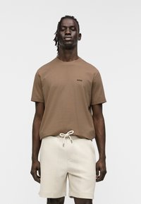 T-shirt en coton marron à manches courtes et col rond, avec un petit logo "BOSS" noir sur la poitrine ; associée à un short texturé crème.