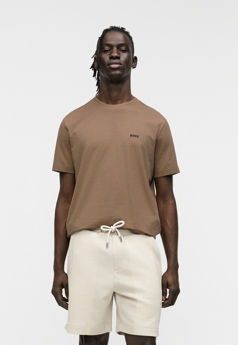 T-shirt en coton marron à manches courtes et col rond, avec un petit logo "BOSS" noir sur la poitrine ; associée à un short texturé crème.