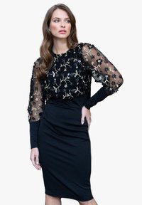 Robe noire avec une silhouette ajustée, manches longues avec un voile brodé transparent, et motifs floraux en or et noir.