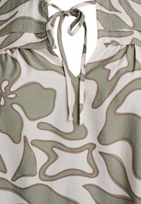 Top a fantasia floreale verde e beige, con scollatura a V, chiusura con fiocco sul retro e tessuto morbido e testurizzato.