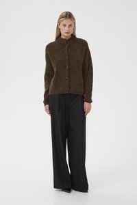 Cárdigan marrón texturizado con cuello alto y cinco botones negros, combinado con pantalones negros holgados, sobre un fondo blanco liso.