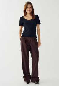 Melnas ribotas īsām piedurknēm tops ar kvadrātveida kakla izgriezumu, kombinēts ar brūnām piegrieztām platām biksēm. Apģērbs rada relaksētu siluetu.