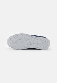 Shoe sole with a textured white rubber surface, featuring a wavy design, circular grip patterns, and a logo embossed on the side.