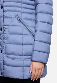 Jasno niebieska kurtka puchowa z pikowaną strukturą, zatrzaskami i ukośną kieszenią na zamek z przodu. Miękki, gładki materiał.