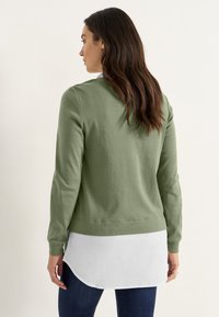 Groene lange mouw top met een ronde hals, voorzien van een witte gelaagde zoom, gemaakt van katoenachtig materiaal, aansluitend ontwerp, gladde textuur.