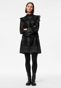 Černé šaty s květinovou výšivkou, volánovými rukávy, vysokým výstřihem a rozšířeným střihem. Nosené přes černé punčochy a masivní černé boty.