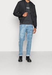 Chaqueta bomber negra sobre una camiseta gris oscuro, jeans azul claro con puños remangados y botas Chelsea negras. Atuendo simple y casual.