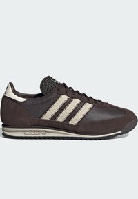 Niskoprofilni crni i bež Adidas tenisice s teksturiranom kožom, suede preklapajući dijelovi, tri bež pruge i brendirani potplat i petni dio.