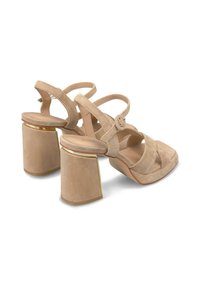 Beige suède high-heeled sandalen met kruislings riemen en gespdetail; vierkante neus en chunky hak met een gouden accent op de basis.