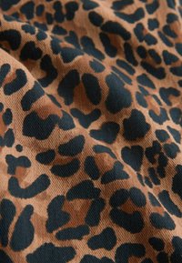 Brūns audums ar melniem neregulāriem leopardu plankumiem, redzama tekstūra un maigas krokas.