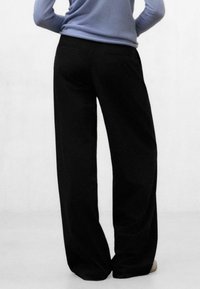 Pantalones de pierna ancha negros, confeccionados con una tela suave, con cintura alta y bolsillos traseros, combinados con una blusa de manga larga azul clara.