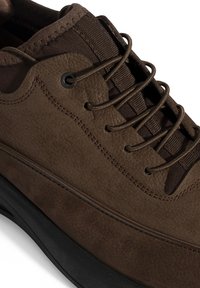 Bruine sneaker met een gladde en gestructureerde leren bovenkant, ronde neus en een donkere rubberen zool. Bevat bruine veters en een gewatteerde tong.