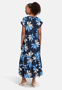 Robe maxi florale en bleu marine avec de grands motifs de fleurs blanches et bleues, manches courtes, bas à volants et tissu léger.
