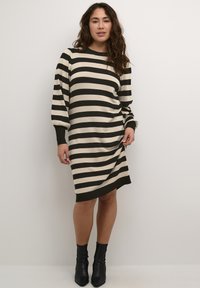 Striped dress featuring horizontal black and cream stripes, long puff sleeves, and a slightly curved hem, paired with black ankle boots.