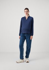 Marineblå langermet topp med V-hals og myk tekstur, kombinert med blå denim jeans og lyse treningssko. Enkel, avslappet passform.