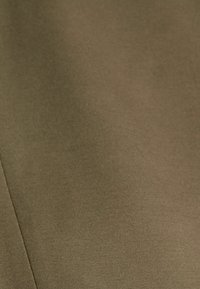 Gros plan sur un tissu vert olive lisse avec une couture verticale sur le côté gauche.
