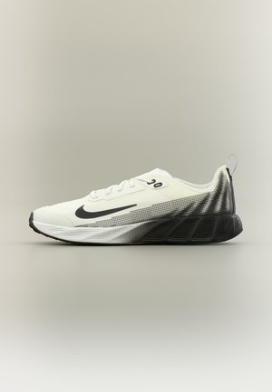 Chaussure de course Nike blanche et noire avec un design à points dégradés sur le talon et une semelle noire, vue de profil sur un fond neutre.