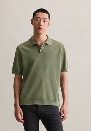 Green knitted polo shirt with a collar, short sleeves, and ribbed hem. Features a textured pattern and side slit detail.
