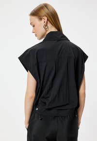 Zwarte short-sleeve shirt met eenstaande kraag, lichtgewicht stof, verlaagde schouders en een relaxte pasvorm. Kenmerkt zich door een gebogen zoom en zilverkleurige hardware.