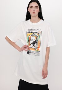 Hvit oversized t-skjorte med fargerik grafikktrykk med reisetema og "Moschino Jeans"-tekst i svart. Korte ermer, laget av bomull.