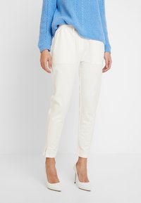 Witte aangesloten broek met zijzakken, getailleerde pasvorm en zijsplitten aan de zoom, gecombineerd met een blauwe gebreide trui en witte hakken.