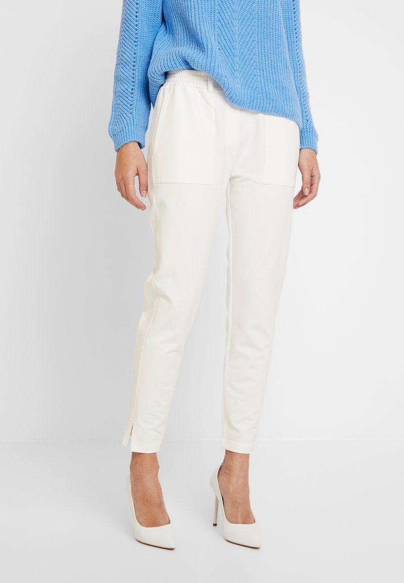 Witte aangesloten broek met zijzakken, getailleerde pasvorm en zijsplitten aan de zoom, gecombineerd met een blauwe gebreide trui en witte hakken.