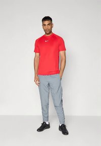 Czerwona sportowa koszulka Nike z krótkimi rękawami, zestawiona z jasnoszarymi spodniami dresowymi z czarnymi paskami po bokach oraz czarnymi butami sportowymi.