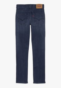 Jeans de denim ajustados color azul oscuro con un acabado texturizado. Cuentan con dos bolsillos traseros y una etiqueta de cuero de la marca en la cintura.