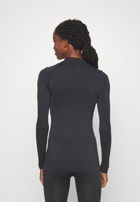 Μακρυμάνικο αθλητικό μπλουζάκι σε μαύρο χρώμα με εφαρμοστή γραμμή, υφασμάτινη υφή, ψηλό γιακά και επίπεδες ραφές για άνεση και ευχέρεια κινήσεων.