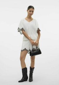 Outfit bianco con orlo a scallop, dettaglio in ricamo nero. Abbinato a una piccola borsa nera e stivali in stile western neri.