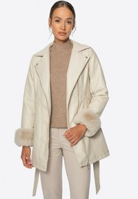 Kremowa skórzana kurtka z futrzanymi mankietami, dopasowany krój, skośny zamek błyskawiczny i kieszenie boczne. Połączona z beżowym golfem w prążki.
