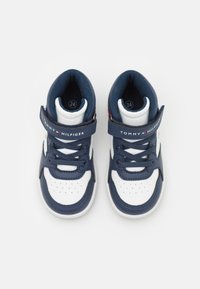 Zapatilla blanca y azul marino con puntera perforada, forro de tela, tira de Velcro y detalles en contraste. Logo en la tira y en la lengua. Talla 24.