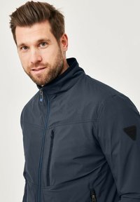 Dark navy jacket with a stand-up collar, front zip closure, and side pockets. Features textured fabric and a logo on the shoulder.