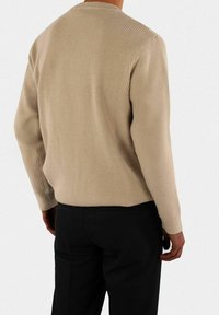 Beige strikket genser med ribbestruktur, rund hals og lange ermer, kombinert med svarte bukser.