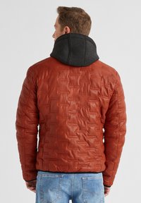 Aufgepolsterte Lederjacke in Rostfarbe mit einem strukturierten Muster und einer schwarzen Kapuze. Merkmale sind der enganliegende Schnitt und die elastischen Bündchen.