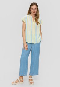 Blouse à manches courtes rayée en jaune pastel, bleu et vert, associée à un jean large bleu clair et des sandales tressées beiges.