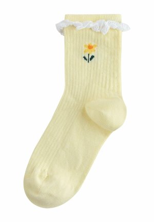Chaussette jaune côtelée avec un volant en dentelle blanche en haut, ornée d'une fleur jaune brodée sur une tige verte près de la cheville.