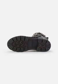 Suela de bota negra con una superficie de goma texturizada, que presenta surcos profundos para un mejor agarre y con el nombre de la marca "REPLAY" grabado en el centro.