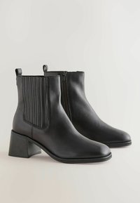 Botas de tobillo de cuero negro con un tacón bajo en bloque, paneles elásticos en los costados, cierre de cremallera y diseño de punta afilada.