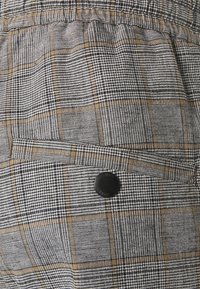 Grå och svart rutigt tyg med en subtil strukturfinish. Har en liten svart knapp på en sidoficka för stängning.