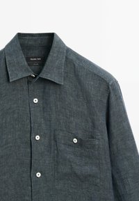 Dark blue linen shirt featuring a spread collar, front pocket, and white buttons. Textured fabric with subtle heathered pattern.